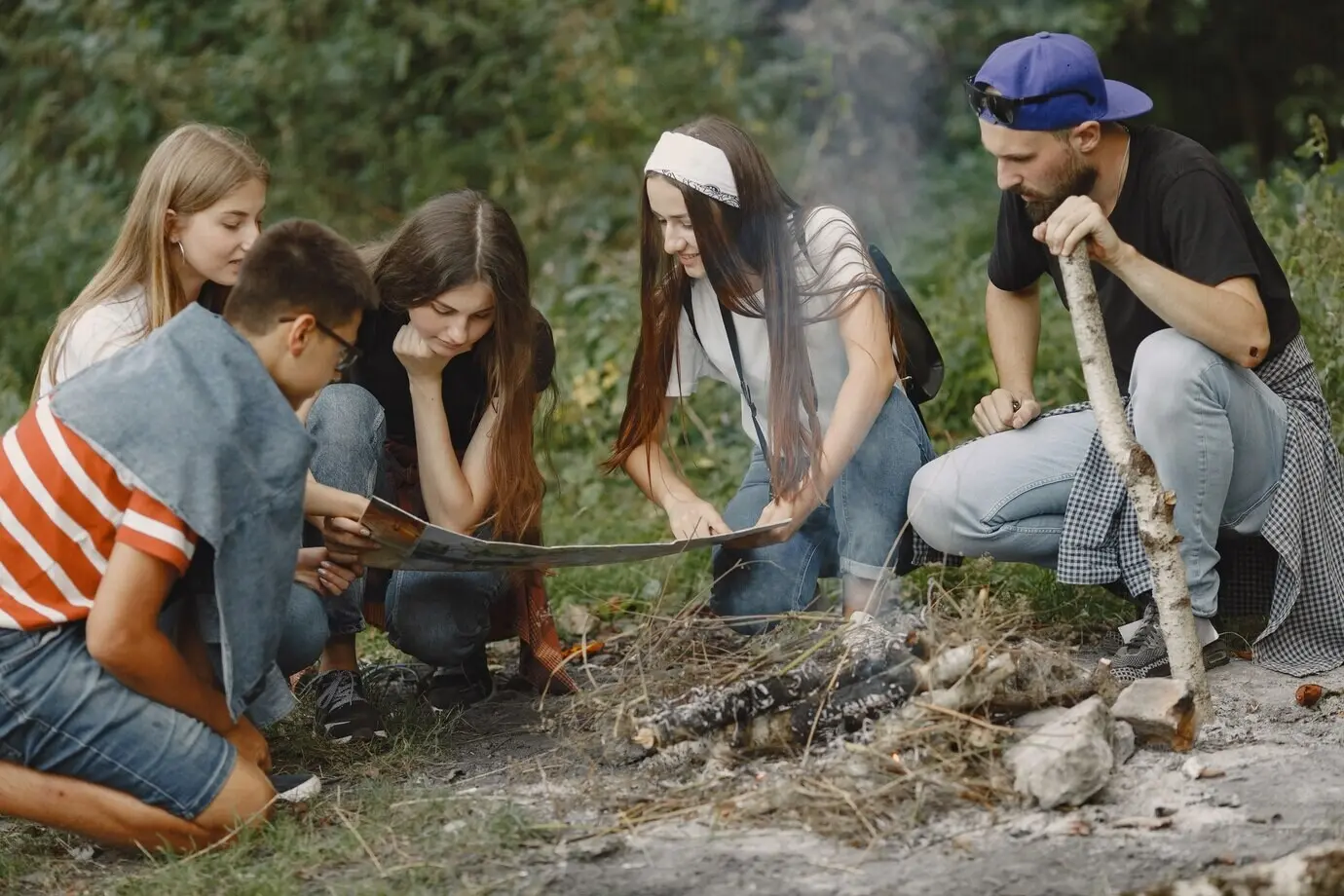 Konzept von Abenteuer, Reisen, Tourismus, Wandern und Menschen. Eine Gruppe lächelnder Freunde in einem Wald. Menschen sitzen in der Nähe eines Lagerfeuers.